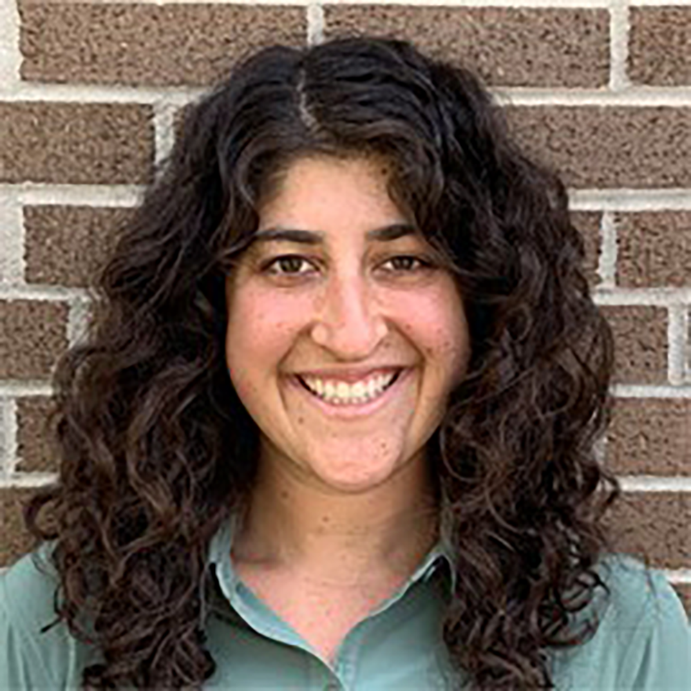 a person with long, curly, dark hair standing in front of a brick wall
