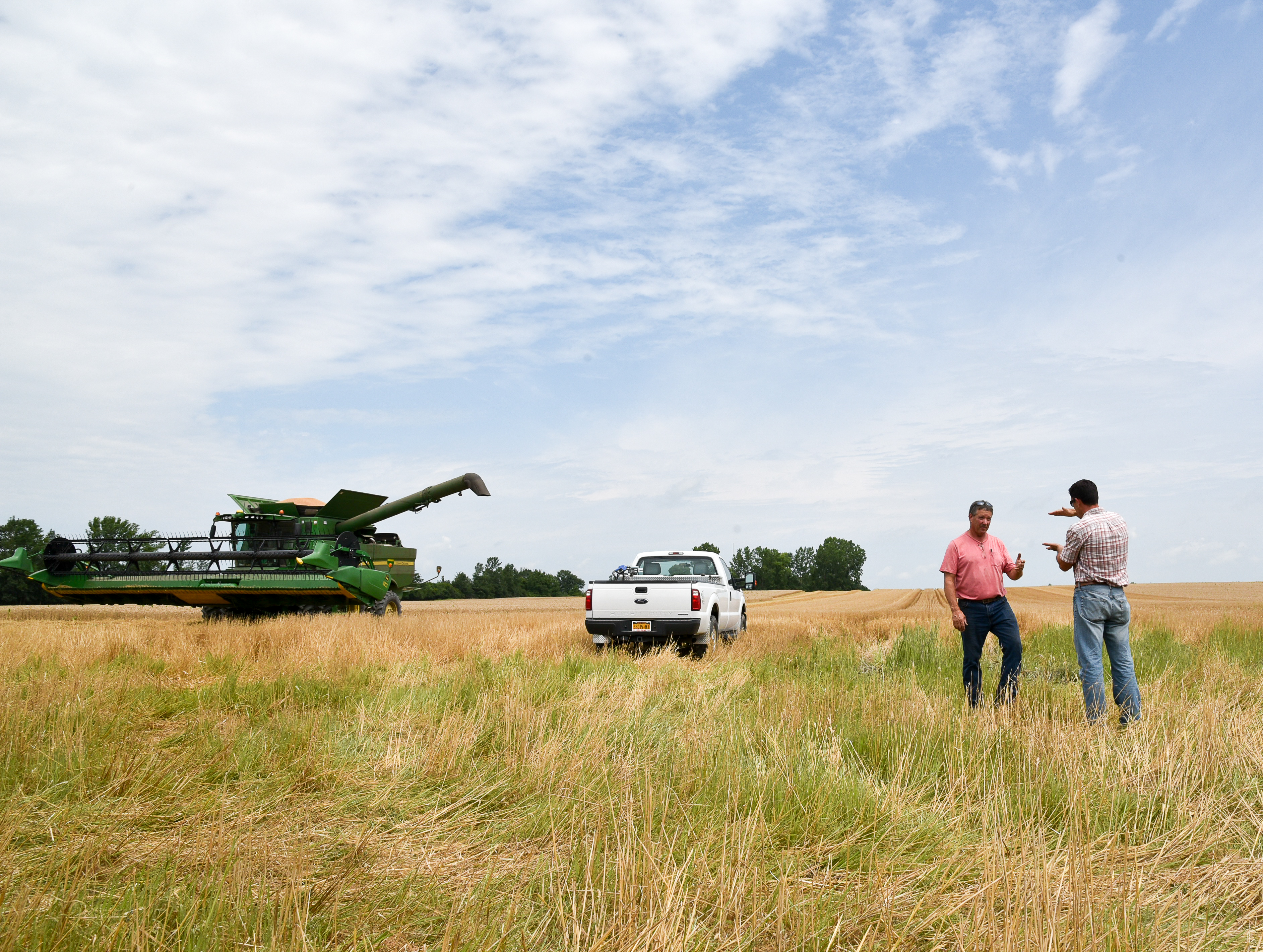 Two men stand near farm equipment in a field