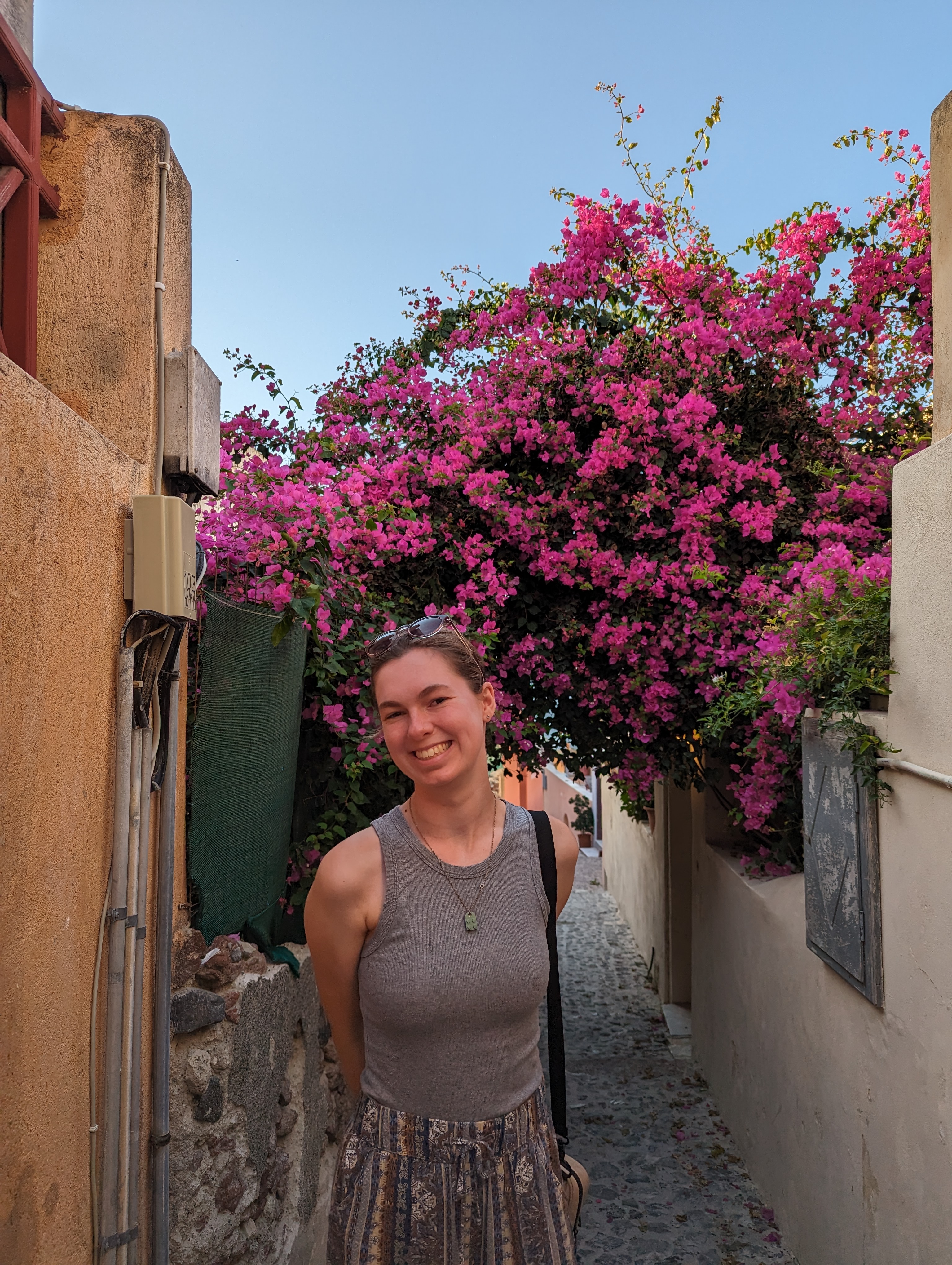 Communications Coordinator, Abby Bravo, standing in front of a bush of pink flowers.