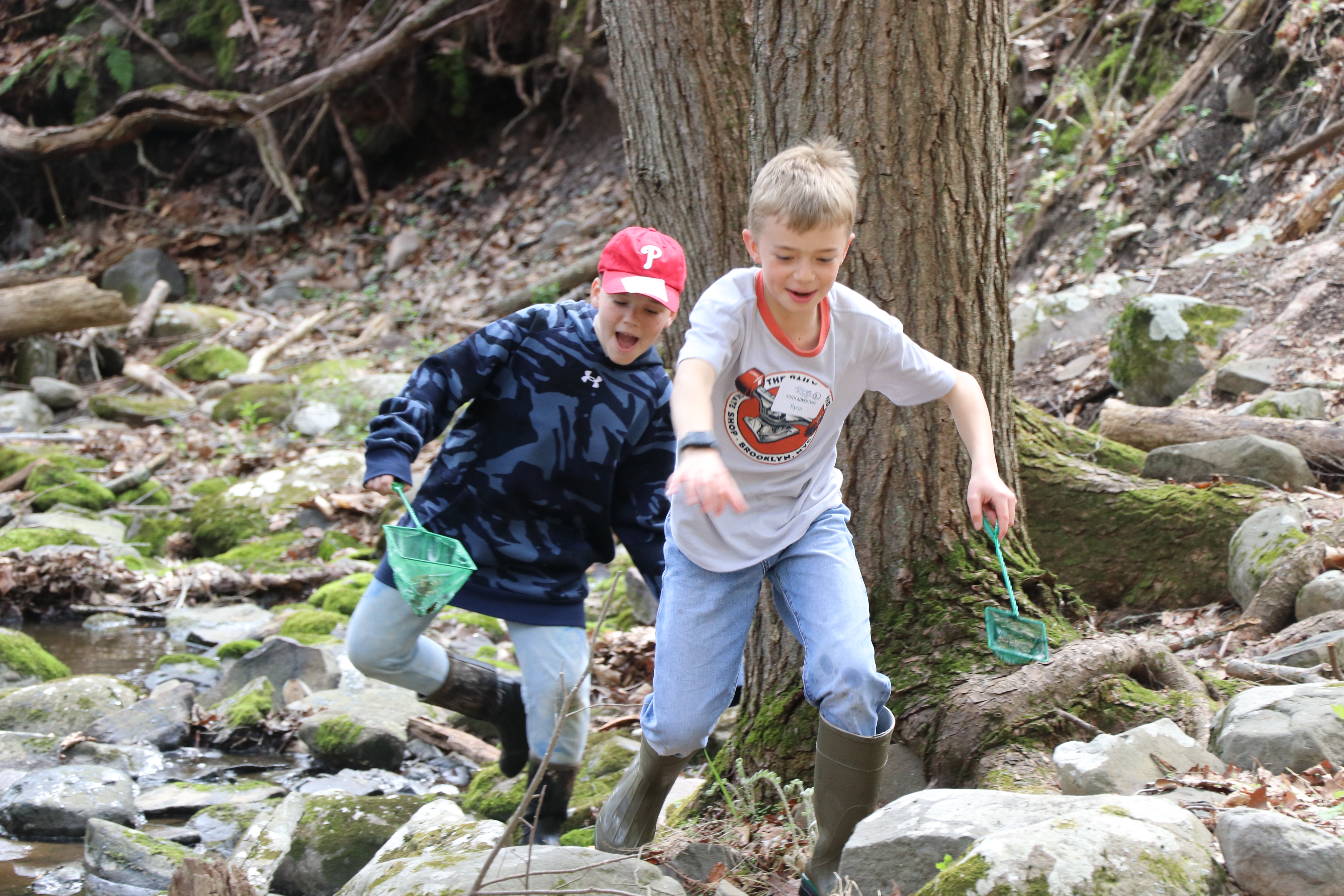 Two young boys run along the edge of a stream looking for crayfish and other macroorganisms.