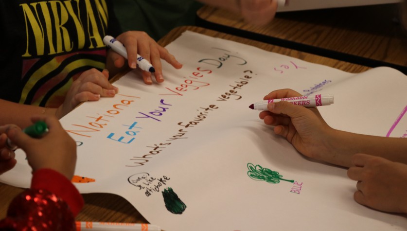 Students write their favorite vegetables down with markers on a large piece of paper.