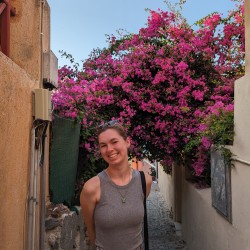 Communications Coordinator, Abby Bravo, standing in front of a bush of pink flowers.