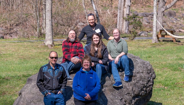 Four people sitting on top of a boulder and two people standing in front of it.