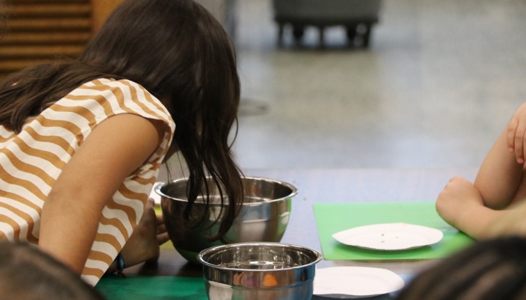 A little girl looks into a metal bowl on a table.
