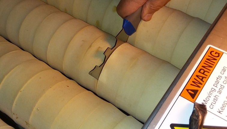 A hand holds a painter's tool, pushing it between absorber foam donuts in a produce washer unit.