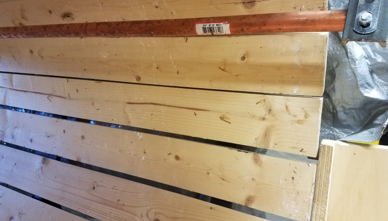 Inside of a root barrel washer with debris on wooden staves and the copper water pipe visible.
