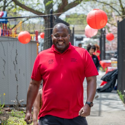 A smiling man in a red polo shirt walks towards the photographer.