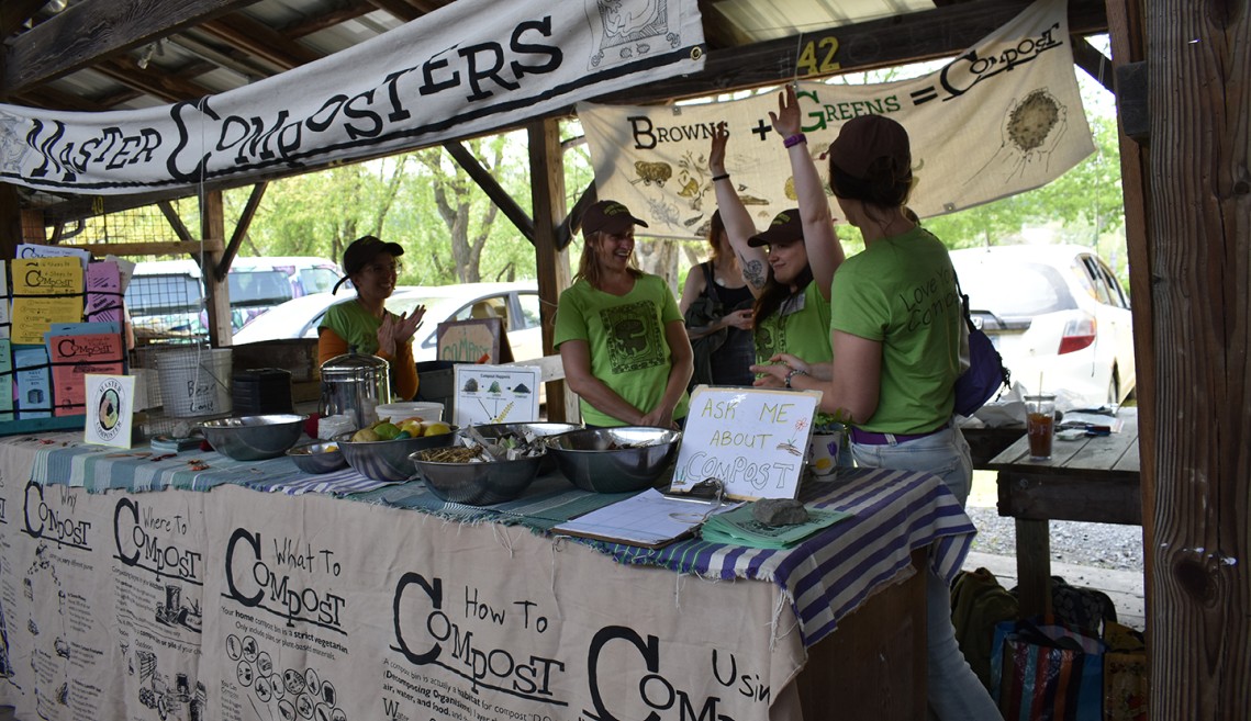 Several volunteers stand in a composting education booth at the Ithaca Farmers Market.
