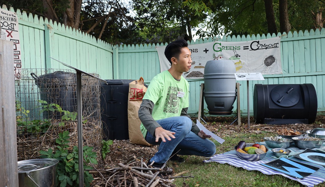 A person crouches next to a pile of sticks and scraps, teaching bird-nest style composting.
