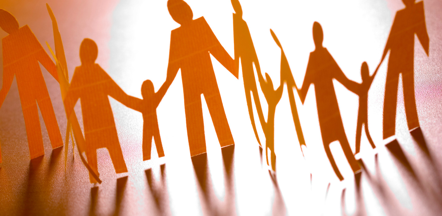 A paper chain of cut-out figures representing adults and children holding hands, backlit with a warm glow