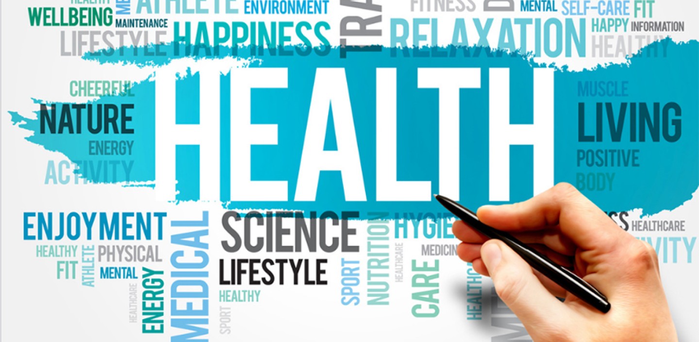 A hand holding a pen hovers over a word cloud with various health and well-being terms.