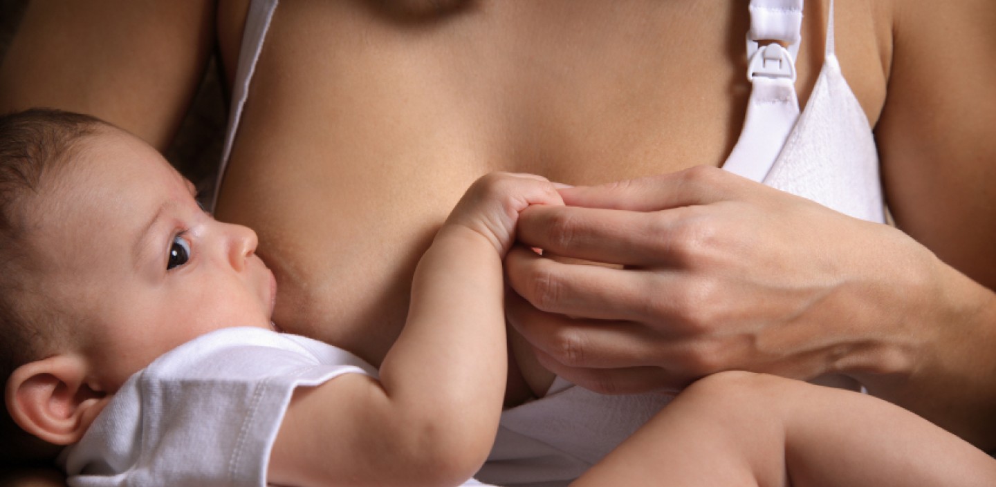 A baby during feeding holding the parent's hand.