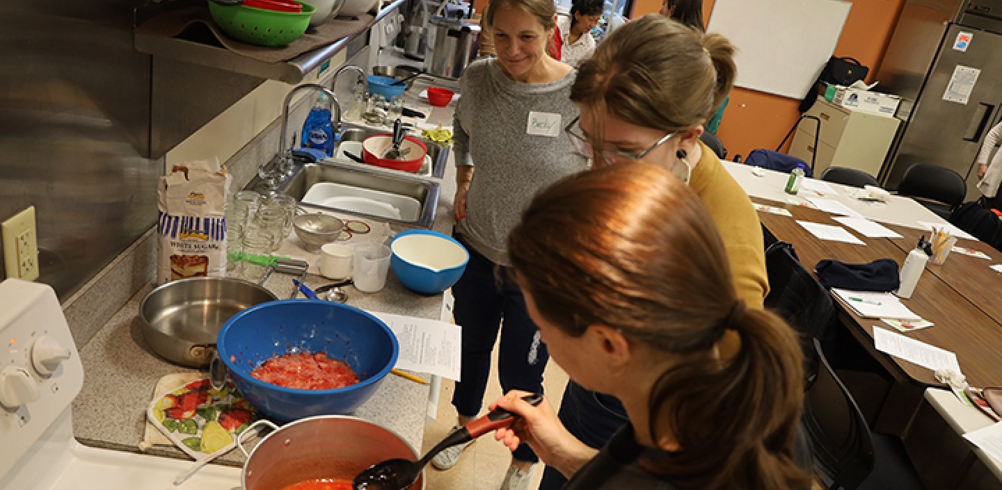 Several people around a stove and countertop making strawberry jam.