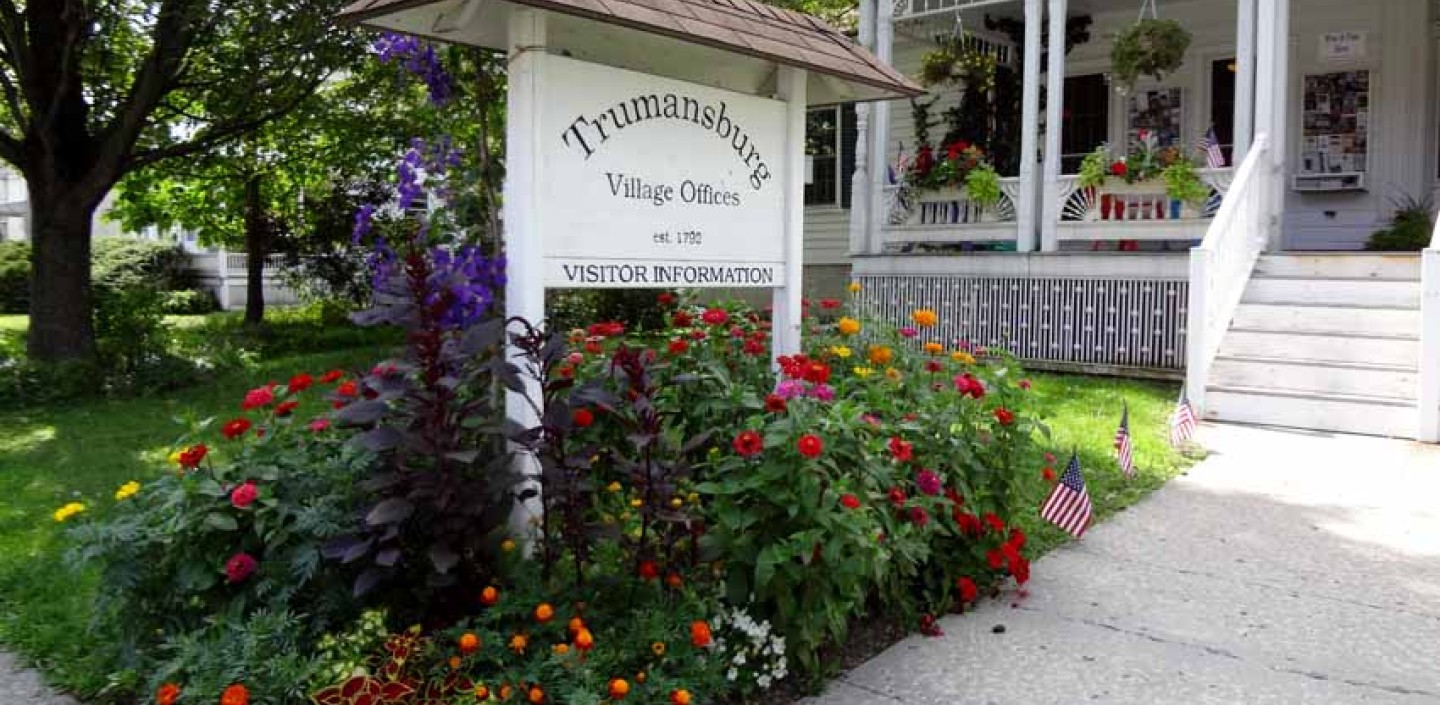 A sign reading Trumansburg Town Hall, surrounded by flowering plants.