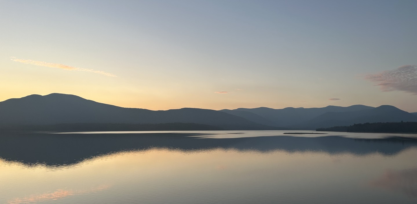 The Ashokan Reservoir at sunset. The mountains are reflecting on the water and the sky is blue and yellow.