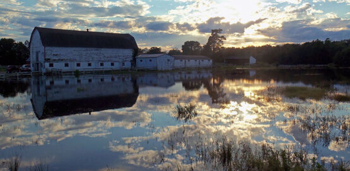 A flooded field near Campbell Hall, NY. The sun is setting and reflecting off the field in front of a barn.