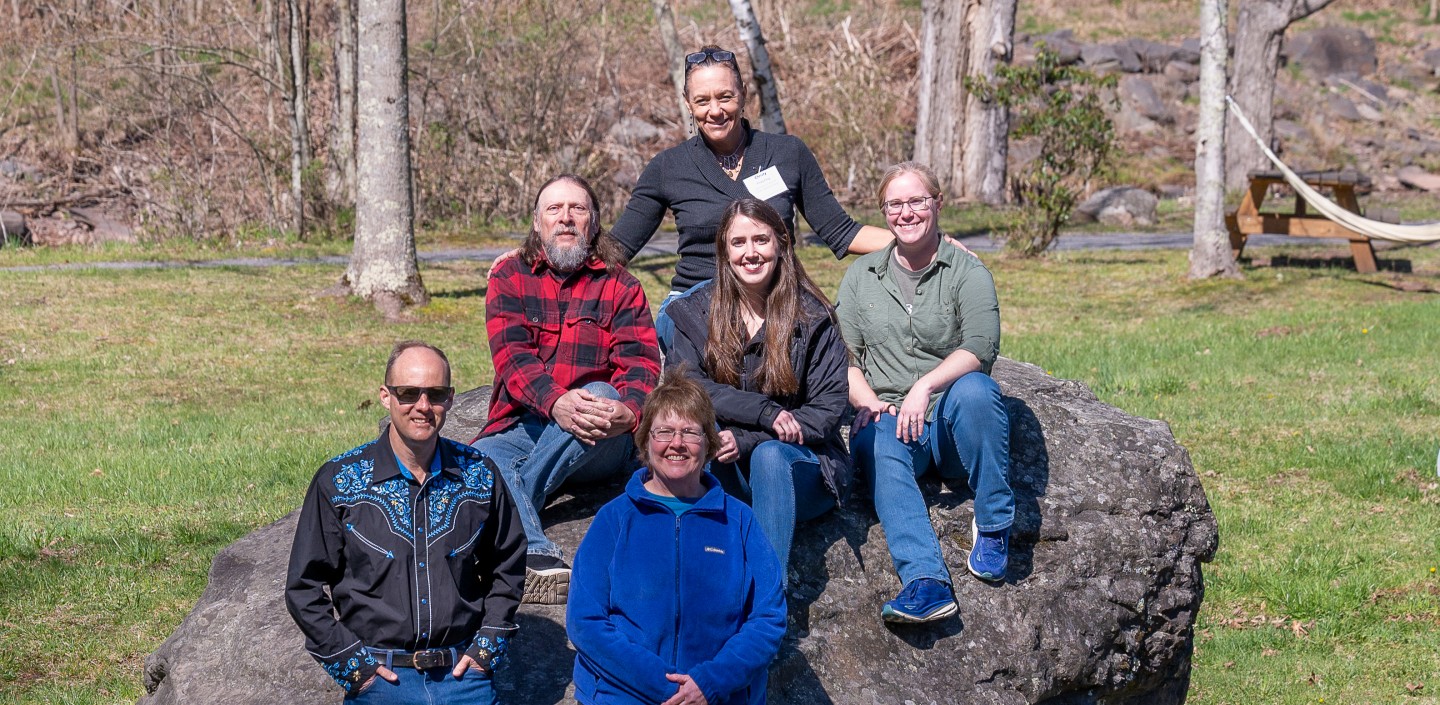 Four people sitting on top of a boulder and two people standing in front of it.