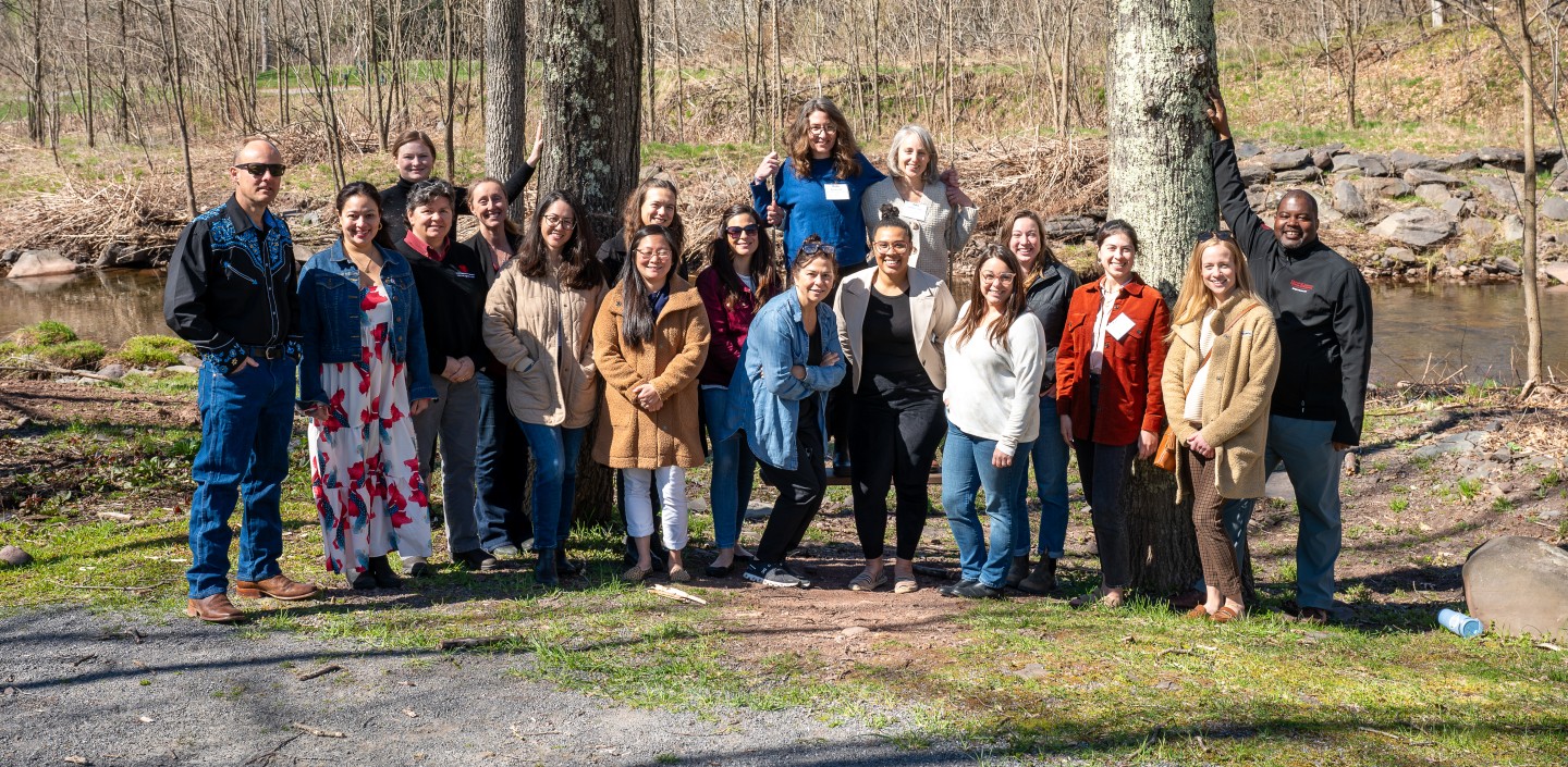Eighteen people pose together for a group photo outside in the fall.