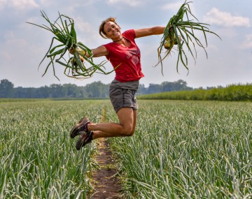 Hoepting holding onions and jumping in an onion field