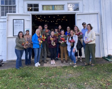 More than a dozen people stand in the doorway of a barn at McCollum Orchards and Gardens. Many are holding cut flower arrangements.