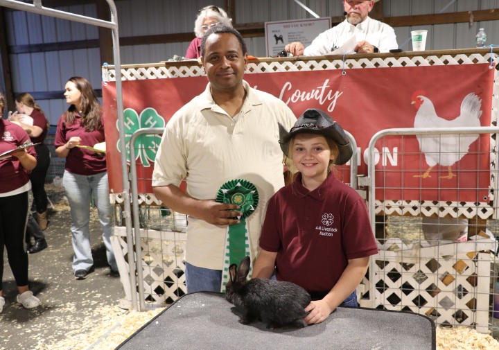 4-H'er, Zoey Pipitone, poses for a photo with one of her auction rabbits and the buyer at the 2025 4-H Livestock Auction.