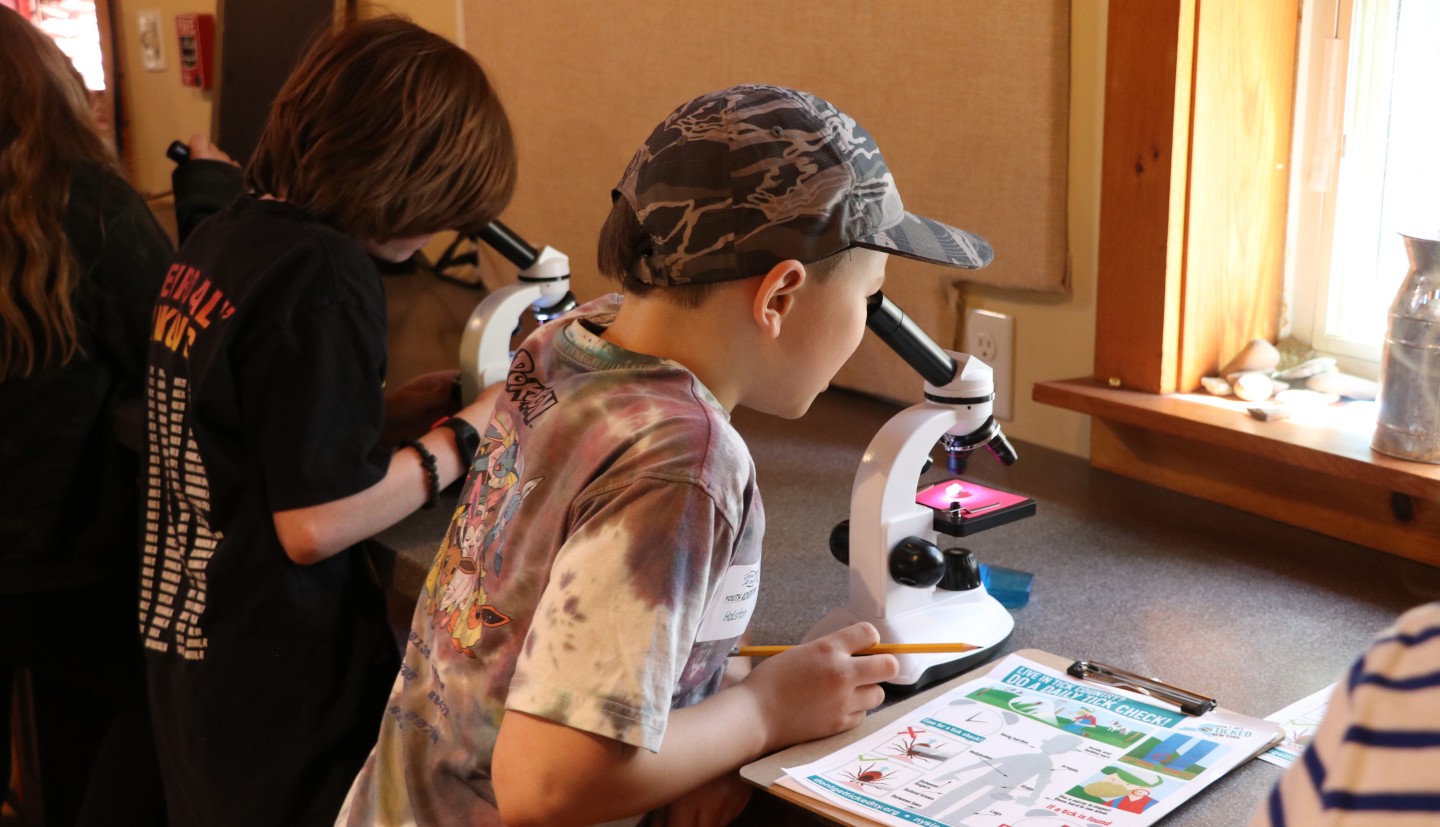 A young boy looks into a microscope with a flyer about tick identification on his right.