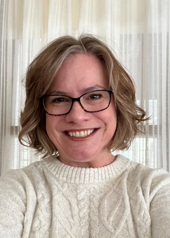 Headshot of Angela Ochterski. She is wearing a cream colored sweater and glasses.