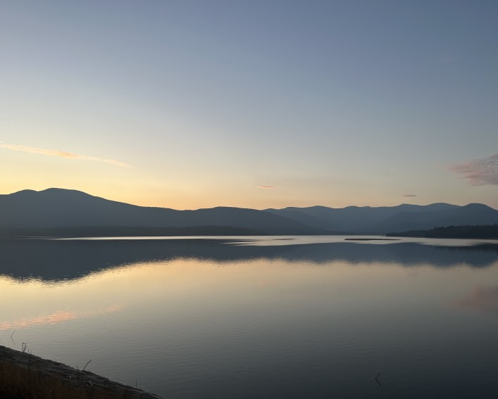 The Ashokan Reservoir at sunset. The mountains are reflecting on the water and the sky is blue and yellow.