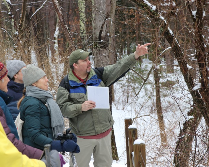 AWSMP Educator, Matt Savatgy, points in the distance during a Snowshoe Stream Walk in February 2026.