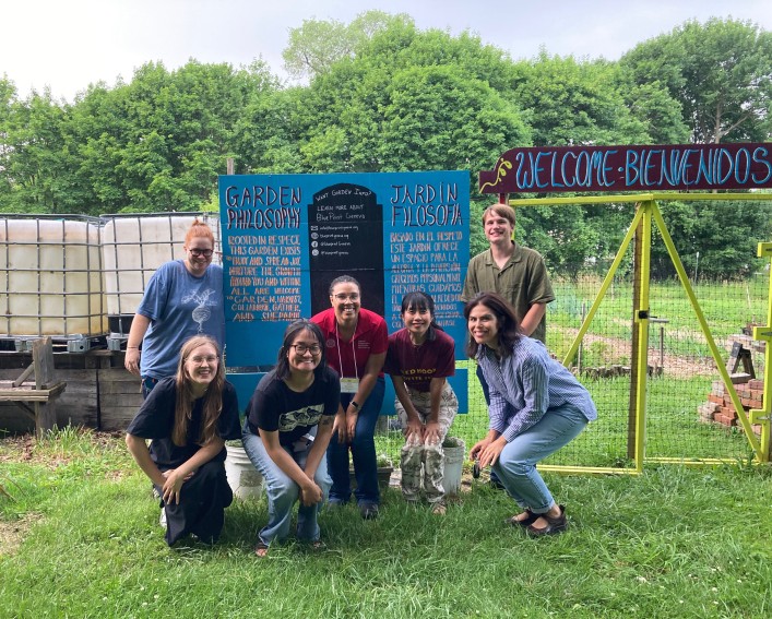 A group of seven people pose together in front of a community garden sign.