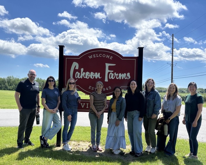 Nine people standing shoulder to shoulder in front of a welcome sign at Cahoon Farms.
