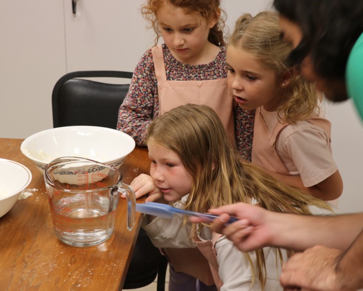 A group of three 4-H'ers measure water in a measuring cup while a 4-H educator explains the measurements..