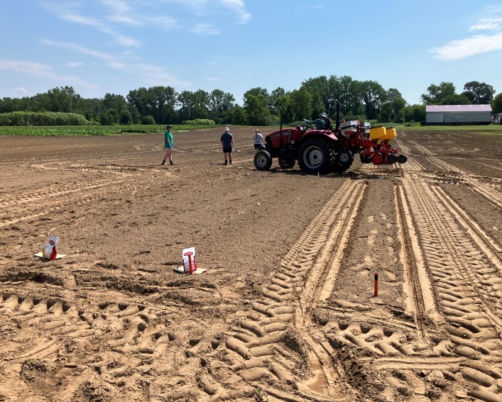Several people setting up a trial on bare soil in a large field. There is red tractor onsite to help with the planting.