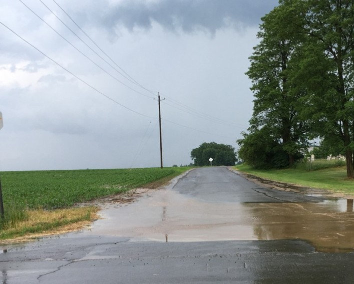 Muddy water running out of a field and ponding on an intersection.
