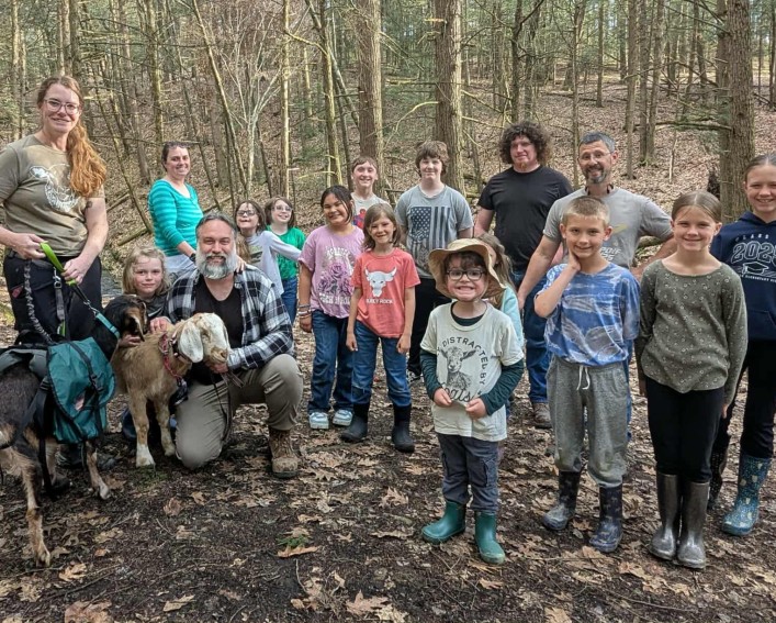 A group of youth enjoying a hike with two goats on leashes