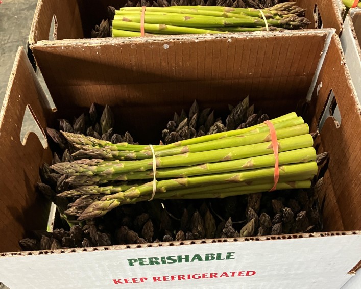 Two boxes of asparagus, each open on the top with a bundle of asparagus laying across the tops of bundles that are standing vertically in the box.