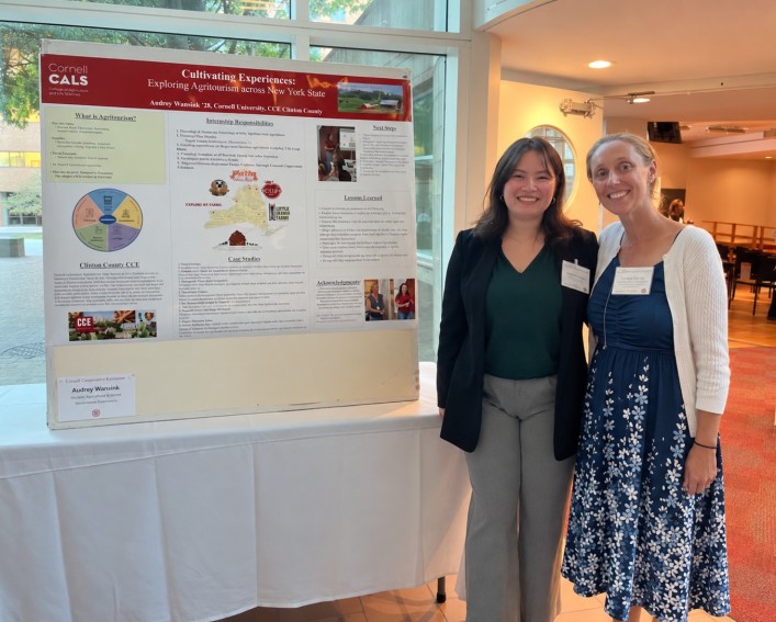Two woman stand next to a Cornell CALS research poster.