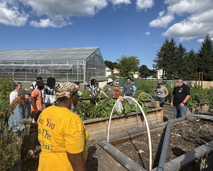 Workshop presenter standing next to empty raised bed outside with hoops in front of group.