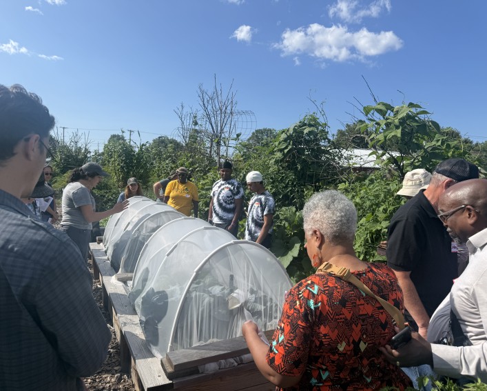 Presenter standing next to raised bed covered with insect netting in front of group.