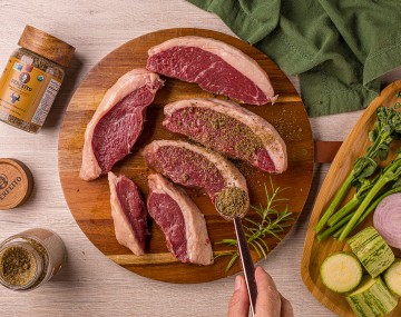 Sprinkling seasoning on a platter of steaks on a wooden cutting board. 