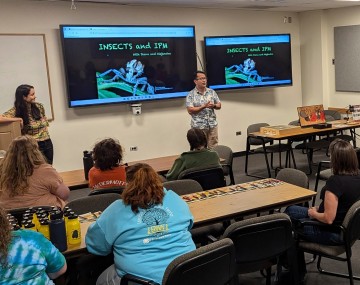 two people in front of a classroom full of students. A screen that says Insects and IPM in the background.