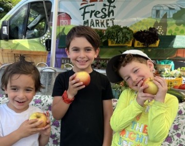 Three kids smile in front of a farm stand
