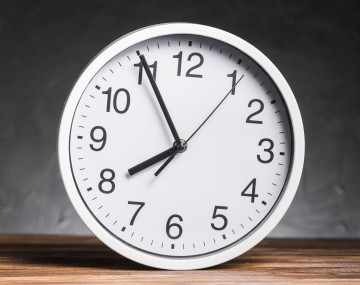 White clock on wooden desk against black background