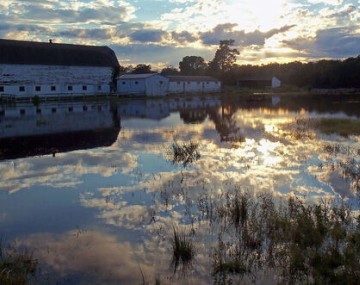 A flooded field near Campbell Hall, NY. The sun is setting and reflecting off the field in front of a barn.