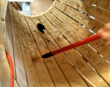 A long red handle with a small brush attached to it is reaching into a wooden root barrel washer. The small brush fits between the staves.