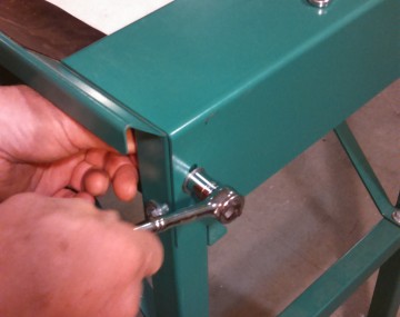 Close up of the end of a conveyor produce washer showing the use of a socket wrench to loosen a bolt.