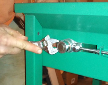 Close up of the end of a conveyor produce washer. An adjustable wrench is being used to loosen the nut on the tension rod.