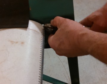Close up of hands holding pliers along the inside edge of a conveyor produce washer near the end of the belt.